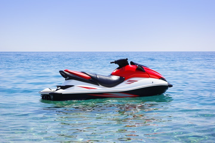 Red and white jet ski floating on calm blue sea under clear sky.