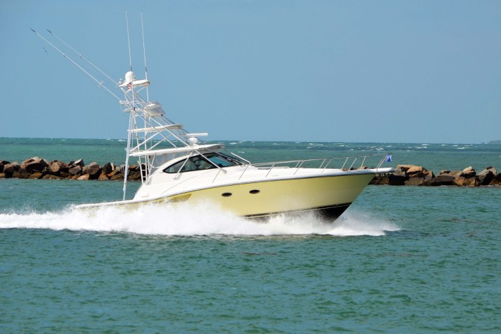 Motorboat with tower cruising on green sea near rocks under clear blue sky.