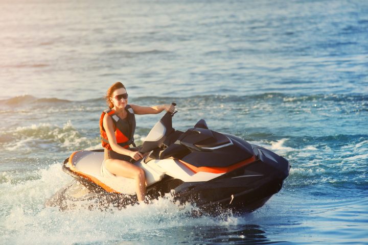 Person riding a jet ski on ocean waves under a sunny sky.