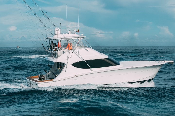 White fishing boat with tall rods on open ocean under a partly cloudy sky.