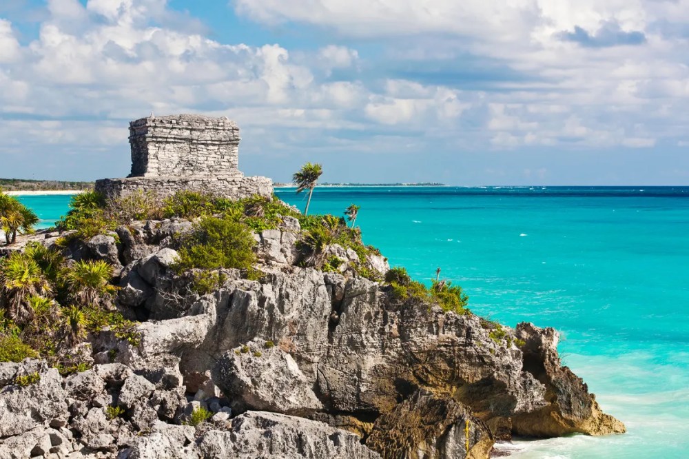 a rocky island in the middle of a body of water with Tulum in the background